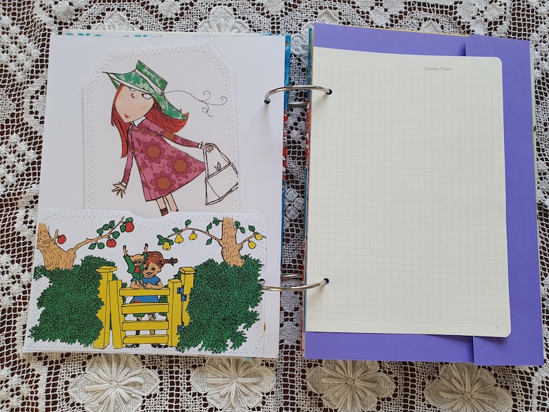 May include: A white binder with a purple cover and a white page with a grid pattern. The binder has a ring mechanism and a decorative floral pattern on the spine. The page has the text "Things I Love" at the top.