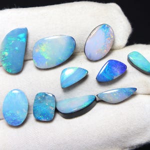 May include: A collection of ten loose, polished opals in various shapes and sizes. These gemstones display iridescent flashes of blue, green, and white light across their smooth, cabochon surfaces, showcasing a vibrant play of color.