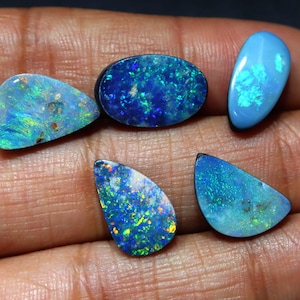 Peut inclure: Cinq opales polies de différentes formes et nuances de bleu et de vert sont présentées. Les opales ont une qualité chatoyante et irisée, avec des éclats de couleur. Les formes comprennent des ovales, des gouttes et des formes libres.