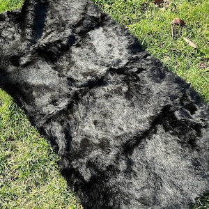 Puede incluir: Una alfombra de piel negra con una textura suave y mullida. La alfombra está colocada sobre una superficie cubierta de hierba.