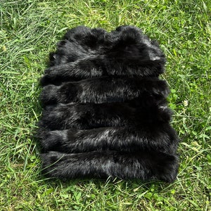 May include: A black fur pelt, likely from a fox, laid out on a bed of green grass.