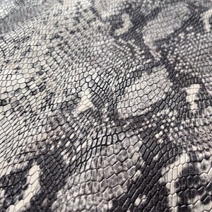 May include: Close-up of a textured fabric with a snakeskin pattern in shades of grey and white.
