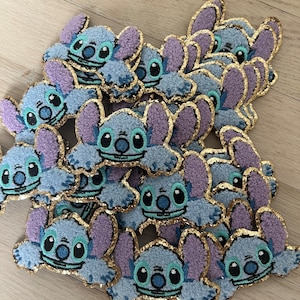 May include: A pile of blue and purple fuzzy Stitch character patches with gold glitter trim. The patches are about 2 inches in diameter.
