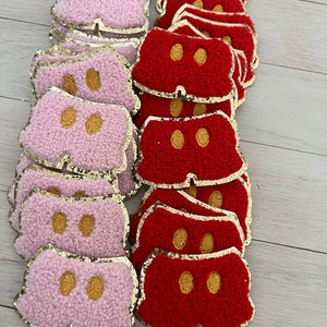 May include: A stack of red and pink fabric Mickey Mouse shorts with gold glitter trim. The shorts are made of a fuzzy material and have embroidered yellow buttons.