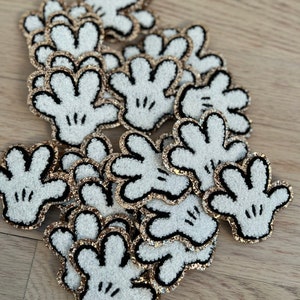 May include: A pile of white felt Mickey Mouse hand patches with black outlines and gold glitter trim.
