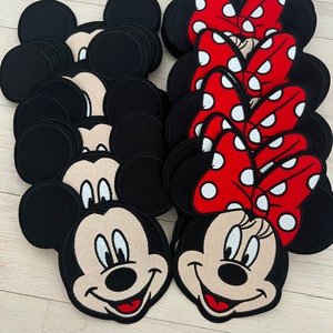May include: A stack of black and white Mickey Mouse and Minnie Mouse character iron-on patches. The Minnie Mouse patches have red bows with white polka dots.