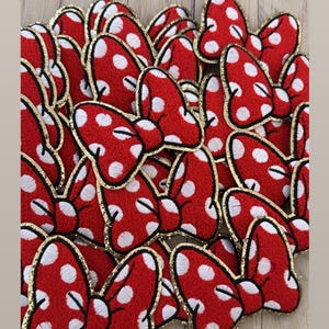 May include: A pile of red and white polka dot bow patches with gold glitter trim. The patches are made of felt and are perfect for adding a touch of whimsy to any project.