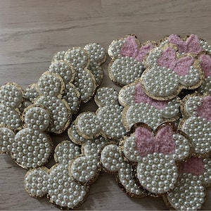 May include: A collection of pink and gold Mickey Mouse head-shaped embellishments covered in white pearl beads.