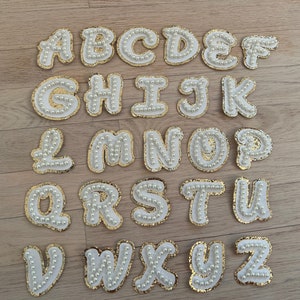 May include: A set of 26 white felt letters with gold trim and pearl embellishments, spelling out the alphabet from A to Z.