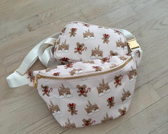 May include: A pink fanny pack and a smaller pink bag with a white strap. Both bags feature a repeating pattern of gingerbread houses and gingerbread bears with red bows.