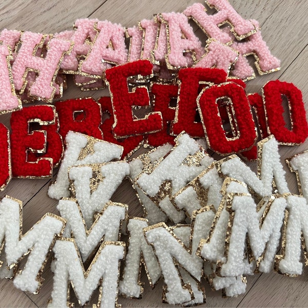 May include: A collection of felt letter patches in pink, red, and white with gold trim. The letters are all uppercase and include the letters M, A, H, E, R, O, and D.