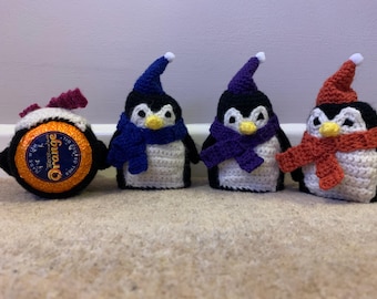 May include: Four crocheted penguin ornaments with different colored scarves. The penguins are white with black heads and beaks. The scarves are blue, purple, red, and orange.