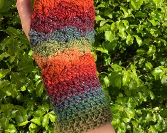 May include: A hand-crocheted fingerless glove in a vibrant array of colours, including orange, red, green, and blue. The textured yarn creates a striped pattern. The glove is designed to cover the wrist and part of the hand.