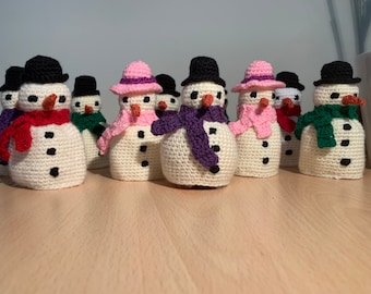 May include: A group of crocheted snowman ornaments with various colored hats and scarves. The snowmen are white with black eyes and buttons.