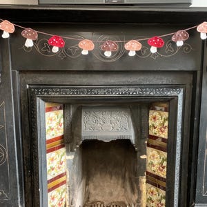 May include: A garland of crocheted mushrooms in shades of red, brown, and white hangs above a black fireplace with decorative tile accents.