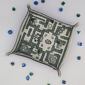 May include: A white fabric dice tray with a brown border and a black and white printed map design. The tray is filled with blue and green dice.