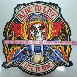 May include: Embroidered patch featuring a skull wearing a helmet, flames, and the text "RIDE TO LIVE" and "LIVE TO RIDE". The patch is approximately 12 inches wide. The design includes a motorcycle and crossed weapons, with a color palette of red, yellow, blue, and black.