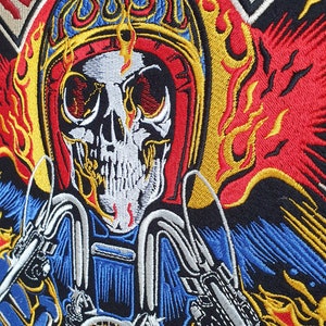 May include: Embroidered patch featuring a flaming skull wearing a motorcycle helmet. The design includes the words "RIDE TO LIVE" and "LIVE TO RIDE" in red, with flames in yellow, red, and blue. The patch is on a black background.