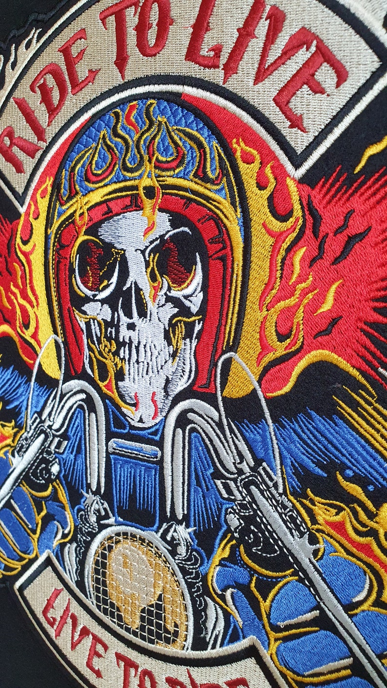 May include: Embroidered patch featuring a flaming skull wearing a motorcycle helmet. The design includes the words "RIDE TO LIVE" and "LIVE TO RIDE" in red, with flames in yellow, red, and blue. The patch is on a black background.