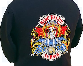 Può includere: Giacca in pile nera con collo alto. La schiena presenta una toppa colorata con un teschio con elmetto, una motocicletta e le parole "RIDE TO LIVE SERBIA". La toppa ha accenti rossi, blu, gialli e bianchi.