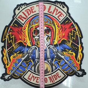May include: Embroidered patch featuring a skull riding a motorcycle, with the text "RIDE TO LIVE" and "LIVE TO RIDE". The patch is approximately 12 inches tall. The design incorporates red, yellow, blue, and black colors, with a detailed, flame-like background.