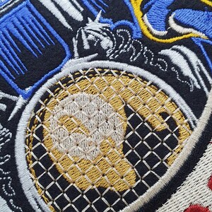 May include: Embroidered patch with a tennis racket design. The patch features a gold and white racket head with a black and white handle. Blue, white, and yellow embroidered details surround the racket, set against a black background.