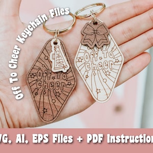 May include: Two wooden keychains with the text "Off To Cheer" and a starburst design. One keychain features a cheerleader megaphone and the other features a bow. The keychains are on a hand.