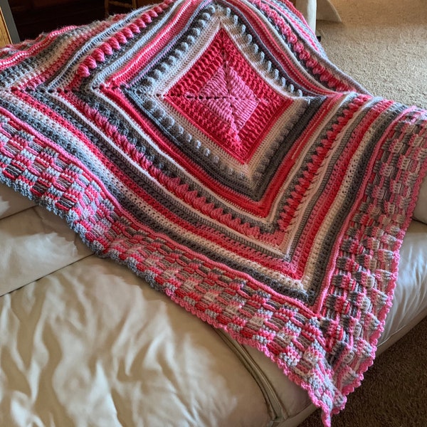 A Beautiful Crocheted Square Afghan of Pink’s, Gray’s, and White.  Created from the pattern “Bernat’s Study of Texture”