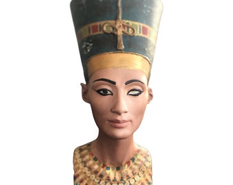 May include: A bust of the Egyptian queen Nefertiti, with a blue and gold headdress and a gold necklace. The bust is made of painted plaster and is a replica of the famous bust of Nefertiti.