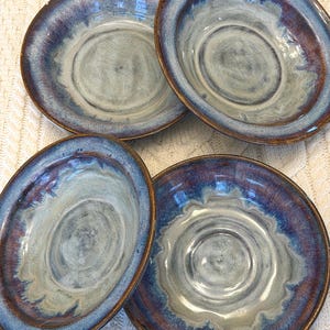 May include: Four ceramic bowls with a blue and brown glaze. The bowls have a circular shape with a slightly raised rim. The interior of the bowls is a light gray color, with a darker blue and brown rim.