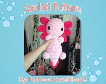 May include: Pink crocheted axolotl plush toy with red gills. The axolotl is being held by a hand. The image has the text "Axolotl Pattern" and "By: PebblesCrochetShop23".