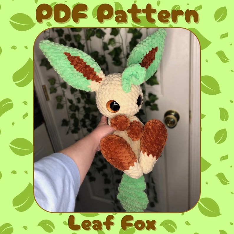 Op de afbeelding: Een gehaakt pluche speelgoed van een Leaf Fox Pokemon. Het speelgoed is bruin, beige en groen. Het speelgoed wordt in de hand van een persoon gehouden.