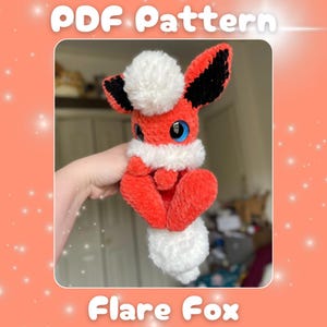 Może przedstawiać: Wzór na szydełku na pluszową zabawkę amigurumi Flare Fox. Lis jest czerwony z białymi akcentami futra i czarnymi uszami. Wzór jest dostępny do pobrania w formacie PDF.