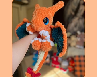 May include: An orange crocheted fire dragon plushie with blue eyes and teal wings. The plushie has white accents on its belly and feet. The image includes the text "PDF Pattern" and "Fire Dragon".
