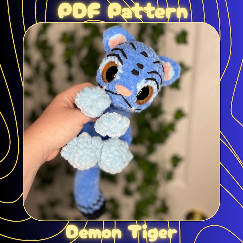 May include: A handmade blue crochet Demon Tiger plushie with light blue accents. The plushie has large brown eyes, black markings, and light blue paws. The text "PDF Pattern" and "Demon Tiger" are visible.