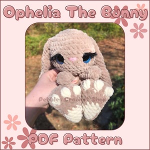 Puede incluir: Un patrón de amigurumi de crochet para un conejito, llamado Ophelia The Bunny, en formato PDF. El conejito es marrón claro con detalles blancos en las patas y tiene ojos azules con pestañas.