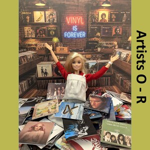 May include: A blonde doll with arms raised, wearing a red long-sleeve shirt and white apron, stands amidst a collection of vinyl record covers. The background features shelves of records and a neon sign that reads VINYL IS FOREVER in blue light.