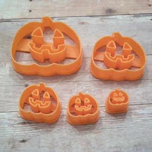 May include: Set of five orange plastic pumpkin cookie cutters of varying sizes. The cutters feature a traditional jack-o'-lantern face design.