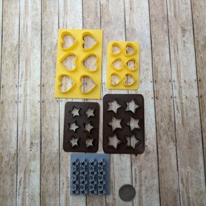 May include: A set of cookie cutters in various sizes and shapes, including hearts and stars. The cutters are made of plastic and are yellow, brown, and gray.