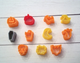 Puede incluir: Un juego de 12 cortadores de galletas con temática de Halloween. Los cortadores están hechos de plástico y vienen en una variedad de colores, incluyendo naranja, amarillo, gris y rojo. Los cortadores presentan diseños como una calabaza, un murciélago, un fantasma, un sombrero de bruja, un ataúd, una calavera, una araña, una luna creciente, un gato y una telaraña.