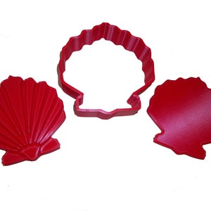 May include: Three red seashell-shaped cookie cutters. One is a complete shell, another is a shell outline, and the third is a solid shell shape. The cutters are made of plastic and are designed for baking or crafting.