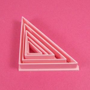 May include: Set of five pink plastic triangle cookie cutters, nested inside each other, with the largest cutter at the bottom.