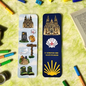 Op de afbeelding: Twee kleurrijke bladwijzers met een blauwe en witte achtergrond. De linker bladwijzer toont een kathedraal, een schelp, een rugzak, een bord en een paar wandelschoenen. De rechter bladwijzer toont een kathedraal, een schelp en de tekst "CAMINO DE SANTIAGO".