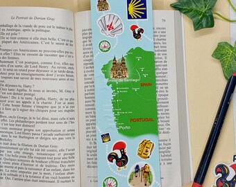 Può includere: Un segnalibro blu e bianco con una mappa del percorso di pellegrinaggio del Camino Portugues. La mappa mostra il percorso da Porto, Portogallo, a Santiago de Compostela, Spagna. Il segnalibro presenta anche illustrazioni di una conchiglia di capesante, un gallo e una freccia gialla.
