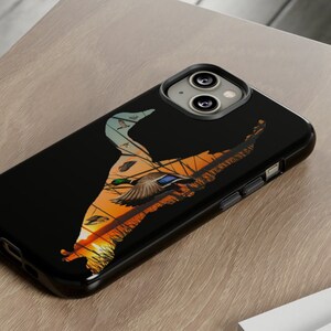 May include: A black phone case with a silhouette of a duck flying over a sunset. The case has a raised camera bump and a cutout for the phone's charging port.