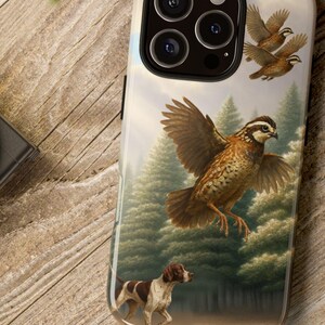 May include: A phone case featuring a detailed illustration of quail in flight above a forest scene, with a hunting dog in the foreground. The case has a glossy finish and a protective design.
