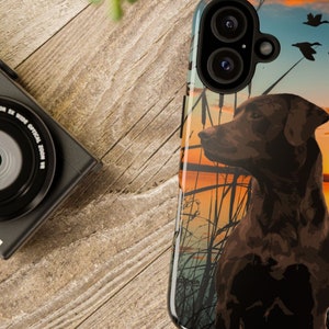 May include: A phone case with a brown labrador retriever silhouette against a sunset background. The dog is standing in a field with tall grass and there are three silhouettes of ducks flying overhead.