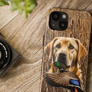 May include: A phone case with a brown and white camouflage pattern featuring a golden retriever dog with a green and blue duck in its mouth.
