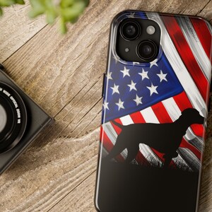 May include: A black phone case with a silhouette of a dog standing in front of an American flag. The flag is red, white, and blue with a distressed look.