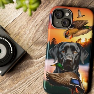 May include: A black Labrador Retriever with a duck in its mouth, set against a sunset background with flying ducks. The image is on a phone case.
